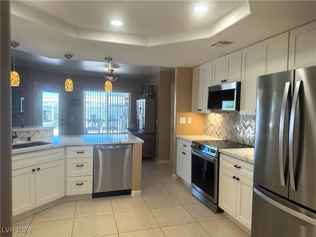 kitchen with white cabinets, pendant lighting, stainless steel appliances, and a tray ceiling