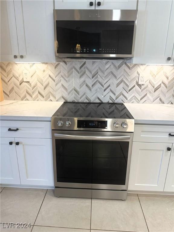 kitchen with light stone countertops, stainless steel appliances, white cabinetry, and light tile patterned flooring