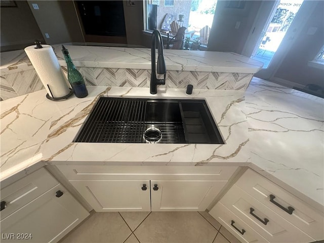 room details featuring decorative backsplash, light stone counters, white cabinetry, and sink