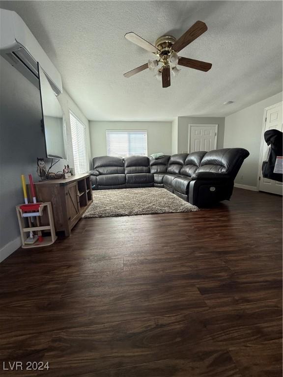 living room with a wall mounted AC, ceiling fan, dark hardwood / wood-style flooring, and a textured ceiling