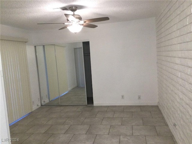 unfurnished bedroom featuring a textured ceiling, tile patterned floors, ceiling fan, and brick wall