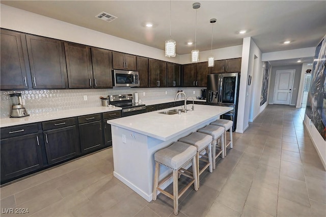 kitchen with a kitchen island with sink, sink, appliances with stainless steel finishes, dark brown cabinetry, and a breakfast bar area