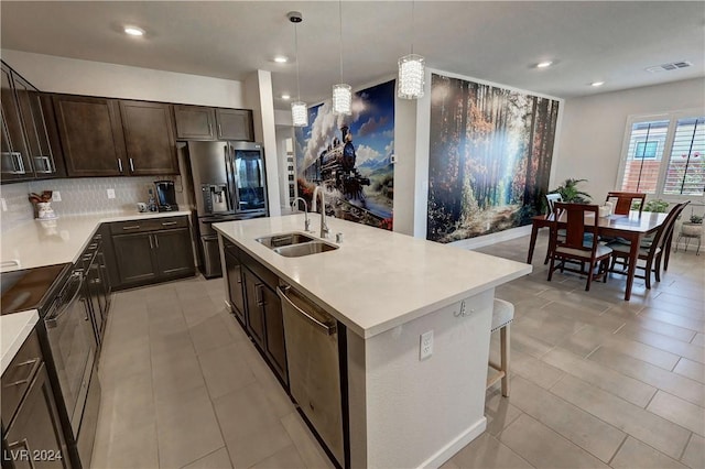 kitchen with pendant lighting, backsplash, a kitchen island with sink, sink, and appliances with stainless steel finishes