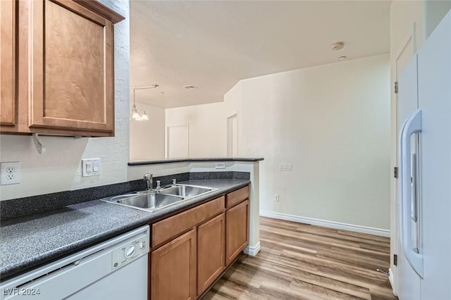 kitchen with pendant lighting, white appliances, sink, hardwood / wood-style flooring, and a notable chandelier