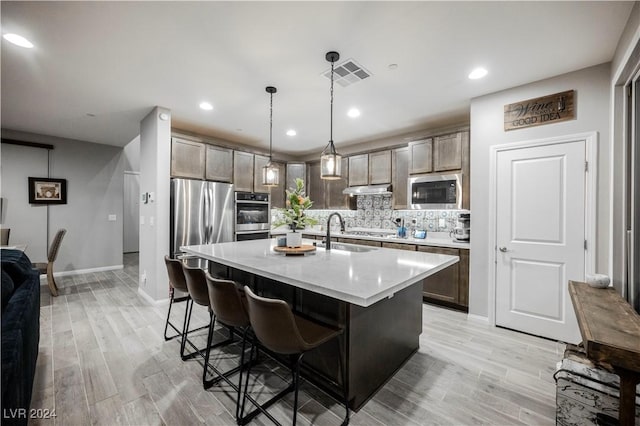 kitchen with built in microwave, an island with sink, sink, backsplash, and hanging light fixtures