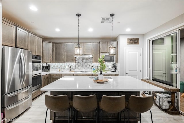 kitchen featuring dark brown cabinetry, stainless steel appliances, decorative light fixtures, and a kitchen island