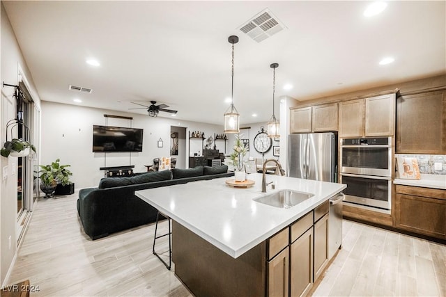 kitchen featuring sink, decorative light fixtures, a kitchen island with sink, stainless steel appliances, and light hardwood / wood-style floors