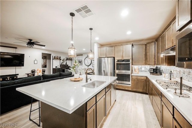 kitchen with sink, decorative light fixtures, stainless steel appliances, and a large island with sink