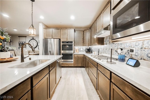 kitchen with sink, tasteful backsplash, hanging light fixtures, light hardwood / wood-style flooring, and appliances with stainless steel finishes