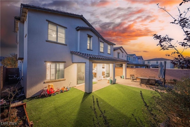 back house at dusk with a lawn and a patio