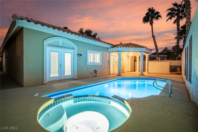 pool at dusk featuring an in ground hot tub, french doors, and a patio