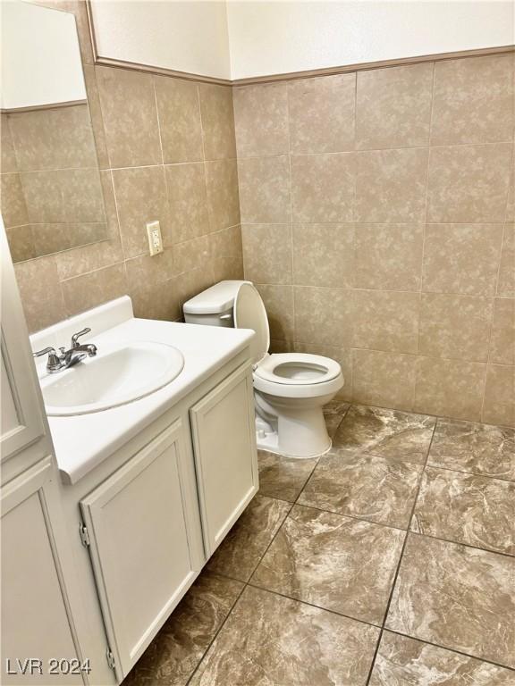 bathroom featuring vanity, tile walls, and toilet