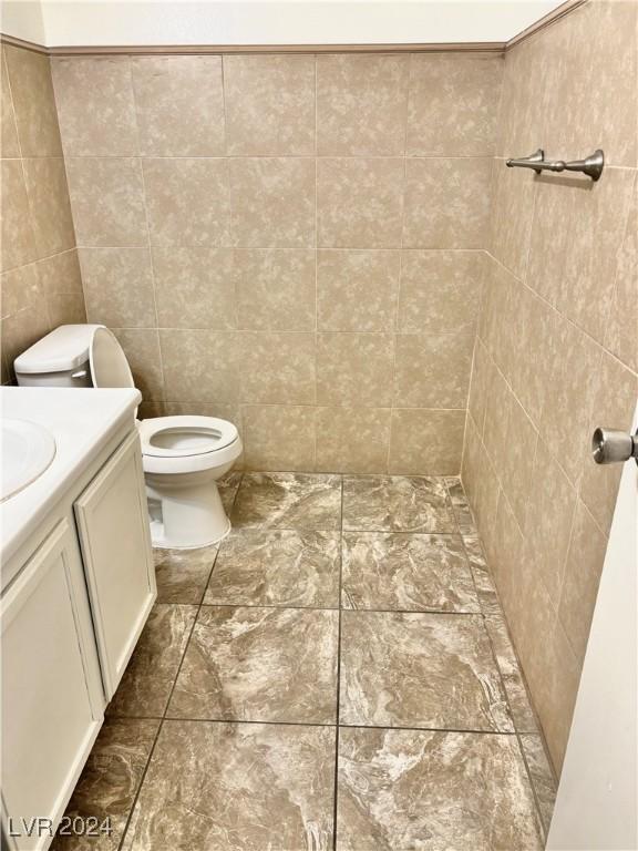 bathroom featuring vanity, toilet, and tile walls