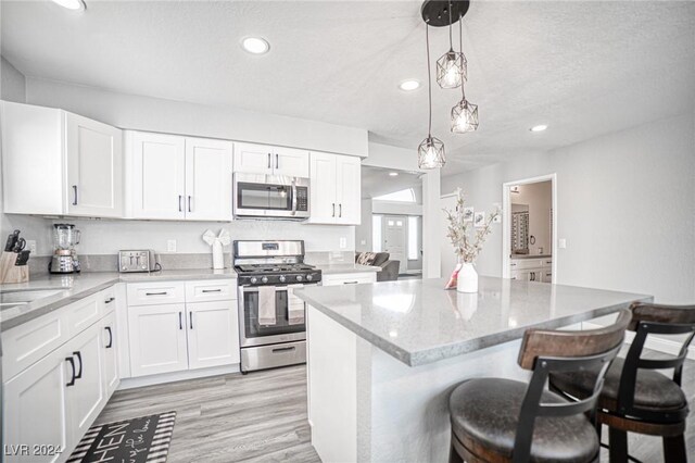 kitchen with white cabinets, decorative light fixtures, light stone countertops, and appliances with stainless steel finishes