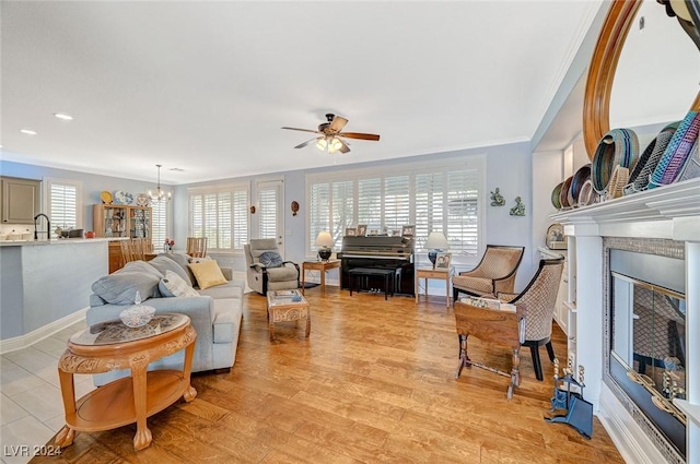 living room featuring a fireplace, ceiling fan with notable chandelier, light hardwood / wood-style floors, and ornamental molding