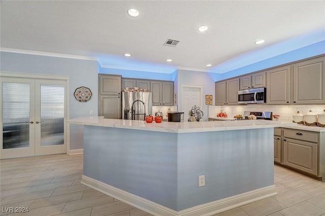 kitchen with french doors, backsplash, stainless steel appliances, and a center island with sink