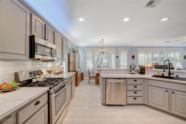 kitchen with backsplash, ceiling fan with notable chandelier, sink, hanging light fixtures, and stainless steel appliances