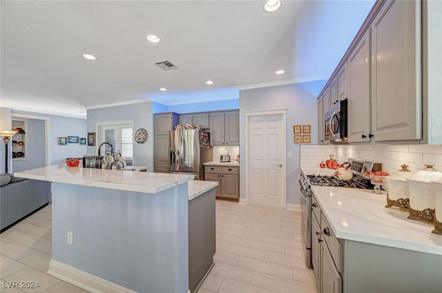 kitchen with stainless steel appliances, tasteful backsplash, gray cabinets, a center island with sink, and ornamental molding