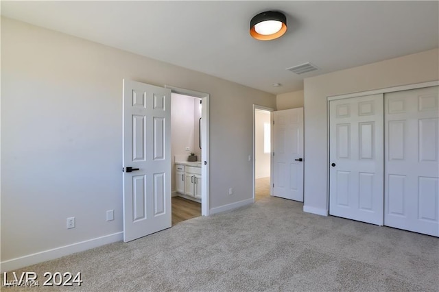 unfurnished bedroom featuring ensuite bathroom, light colored carpet, and a closet