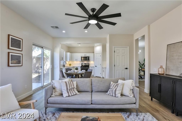 living room with light hardwood / wood-style flooring, ceiling fan, and sink