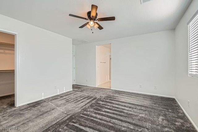 unfurnished bedroom featuring a walk in closet, carpet floors, a closet, and ceiling fan