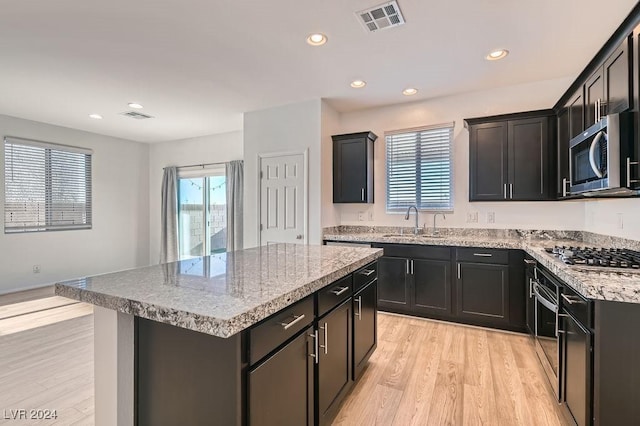 kitchen featuring sink, light stone counters, light hardwood / wood-style floors, a kitchen island, and appliances with stainless steel finishes