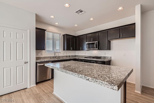 kitchen with stone counters, a center island, stainless steel appliances, and light hardwood / wood-style floors