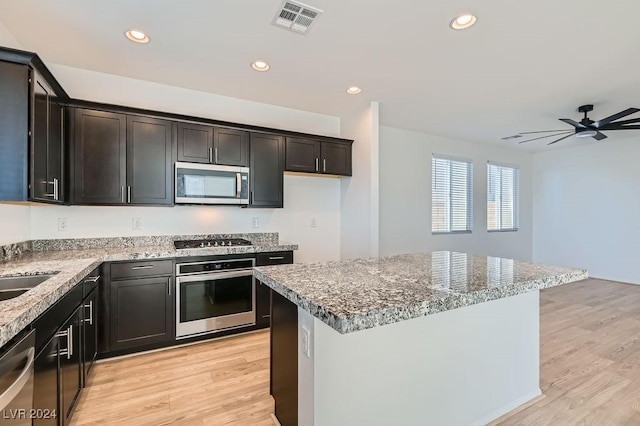 kitchen featuring light stone counters, stainless steel appliances, ceiling fan, light hardwood / wood-style flooring, and a kitchen island