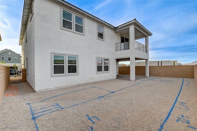 rear view of house with a balcony, a fenced backyard, and stucco siding