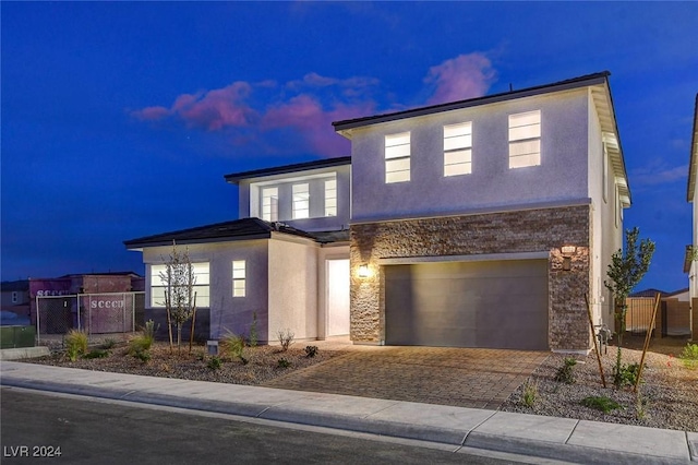 view of front of home featuring decorative driveway, stone siding, fence, and stucco siding