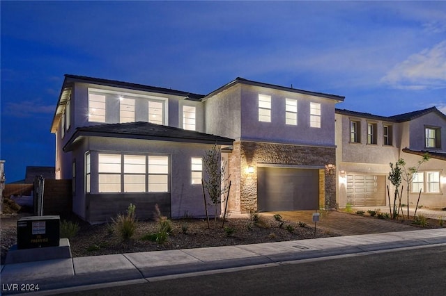 view of front of home featuring decorative driveway, stone siding, an attached garage, and stucco siding