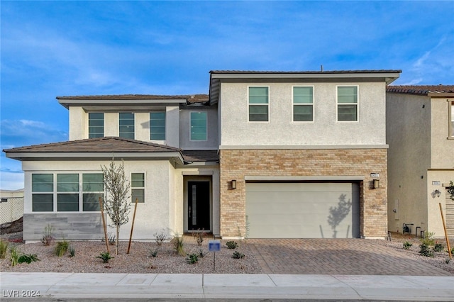 view of front facade featuring a garage, decorative driveway, brick siding, and stucco siding