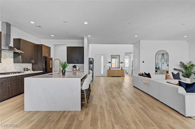 kitchen featuring gas cooktop, open floor plan, light countertops, black fridge, and wall chimney exhaust hood