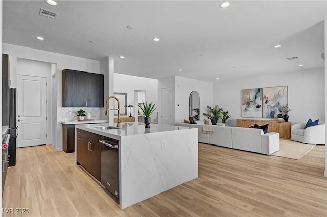 kitchen with light wood-style floors, visible vents, a sink, and a center island with sink