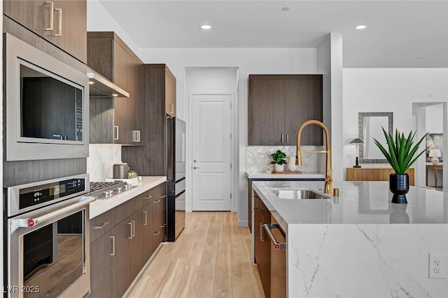 kitchen with decorative backsplash, light wood-style flooring, appliances with stainless steel finishes, ventilation hood, and a sink