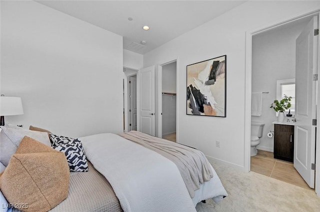 bedroom featuring light colored carpet, a spacious closet, baseboards, and ensuite bathroom