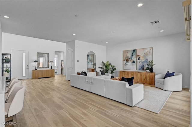 living room featuring arched walkways, recessed lighting, visible vents, and light wood-style flooring