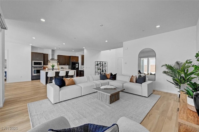 living area featuring arched walkways, recessed lighting, light wood-style flooring, and baseboards