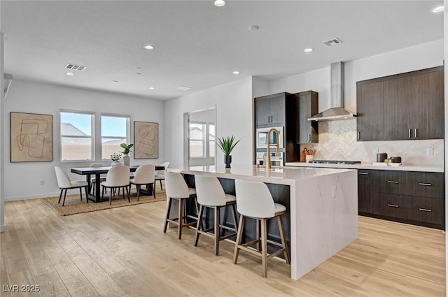 kitchen featuring a kitchen island with sink, wall chimney exhaust hood, visible vents, and stainless steel appliances