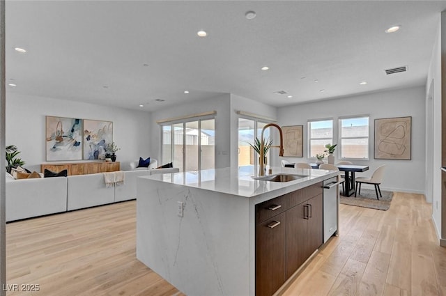 kitchen featuring dark brown cabinetry, a kitchen island with sink, light wood-style floors, a sink, and recessed lighting