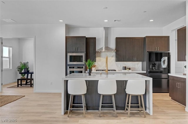 kitchen featuring wall chimney range hood, smart refrigerator, a kitchen bar, and stainless steel microwave