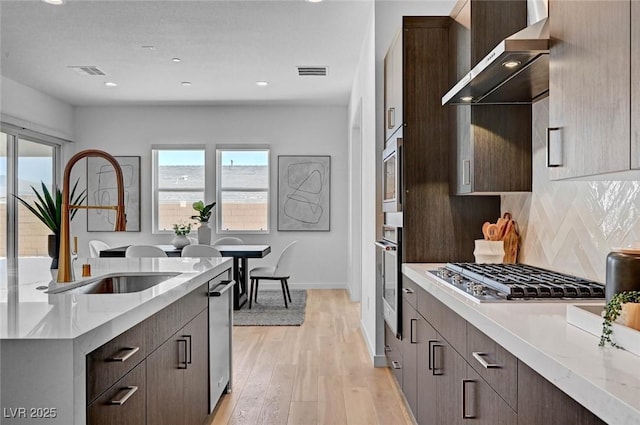 kitchen with visible vents, wall chimney exhaust hood, appliances with stainless steel finishes, dark brown cabinets, and a sink