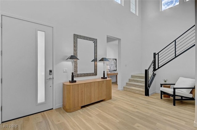 foyer entrance with stairs, light wood-type flooring, a towering ceiling, and baseboards