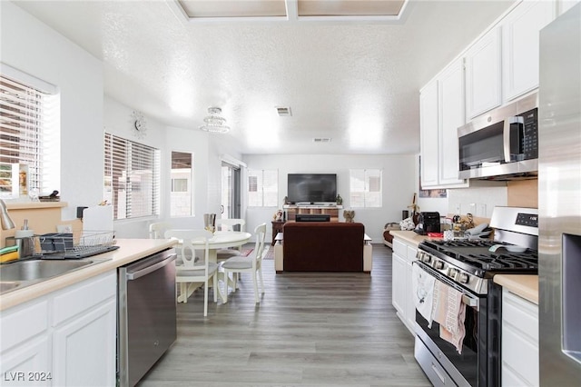 kitchen featuring a textured ceiling, stainless steel appliances, white cabinetry, and light hardwood / wood-style flooring