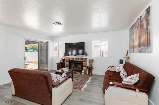 living room featuring light hardwood / wood-style floors, a textured ceiling, and a brick fireplace