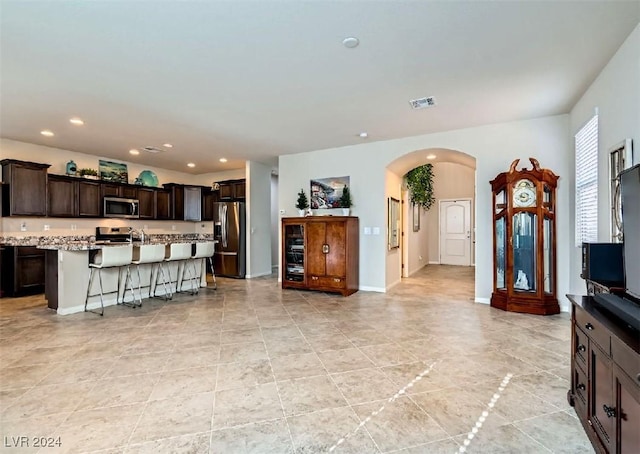 kitchen with a breakfast bar, appliances with stainless steel finishes, dark brown cabinets, a kitchen island, and light stone counters