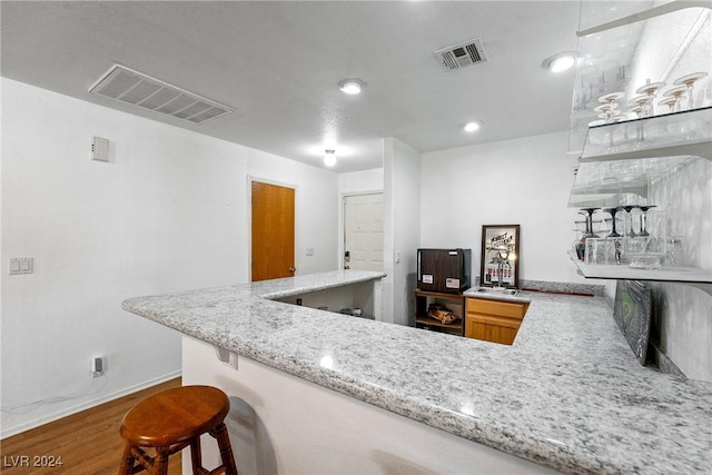 kitchen with hardwood / wood-style flooring, a kitchen breakfast bar, light stone countertops, and kitchen peninsula