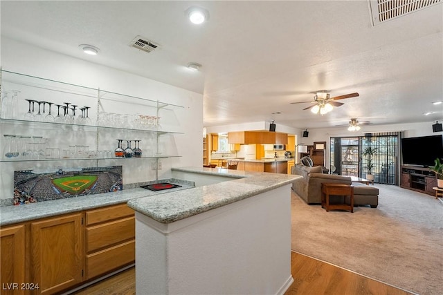 kitchen with kitchen peninsula, ceiling fan, light stone countertops, and light wood-type flooring