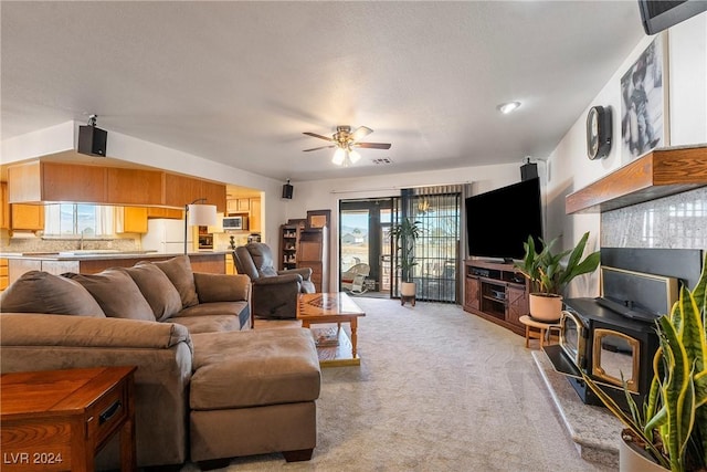 carpeted living room with a wood stove, ceiling fan, and sink