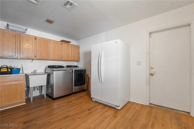 clothes washing area with washing machine and clothes dryer, sink, cabinets, a textured ceiling, and light wood-type flooring